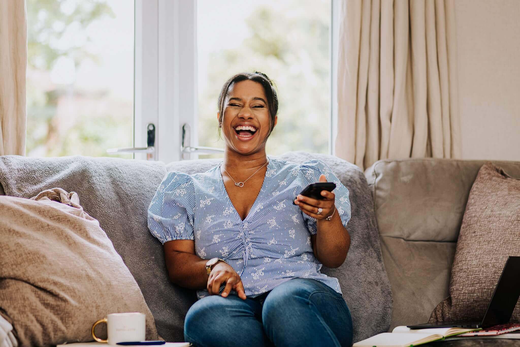 Chanelle, founder of Core People Solutions, laughing on a sofa at home with her phone